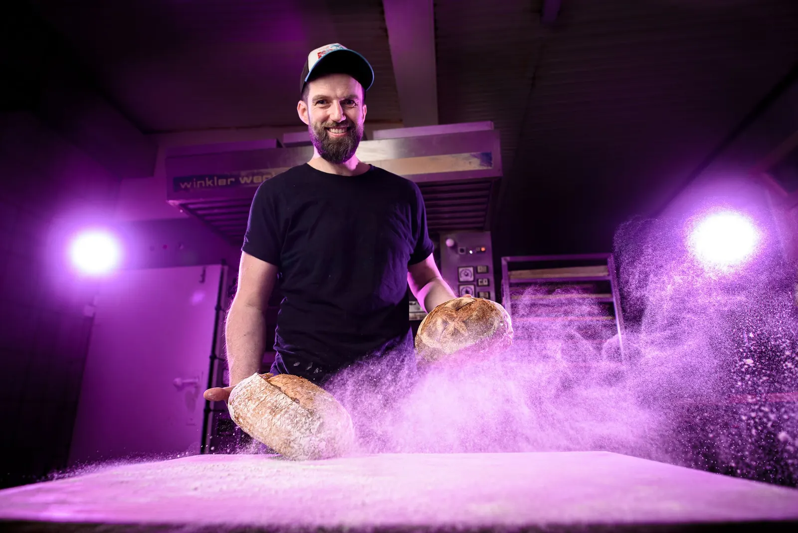 Handwerk mit Stimmung Bäckermeister Manuel Dietrich mit Brot und Mehlstaub in violettem Licht, Imagefoto für seine Handwerksbäckerei